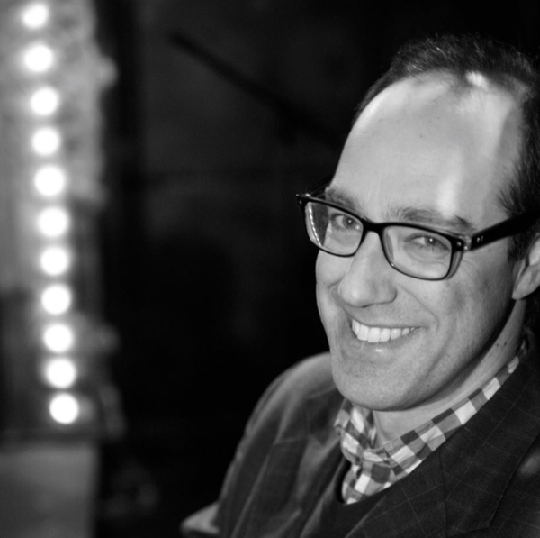 Portrait of Joel Abbott, backstage dressing-room mirror lights blurred behind him