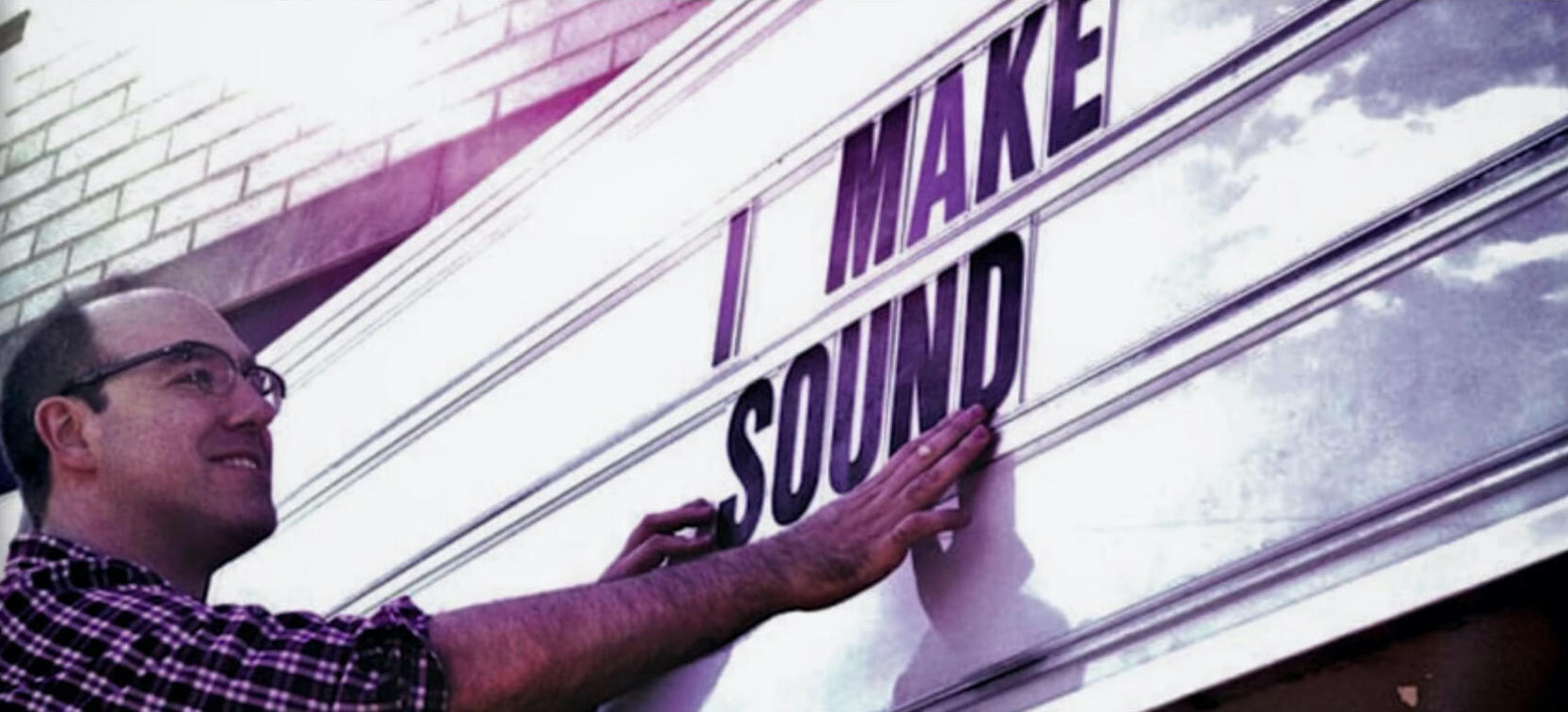 Joel Abbott touching up a theatre marquee sign that reads "I Make Sound"